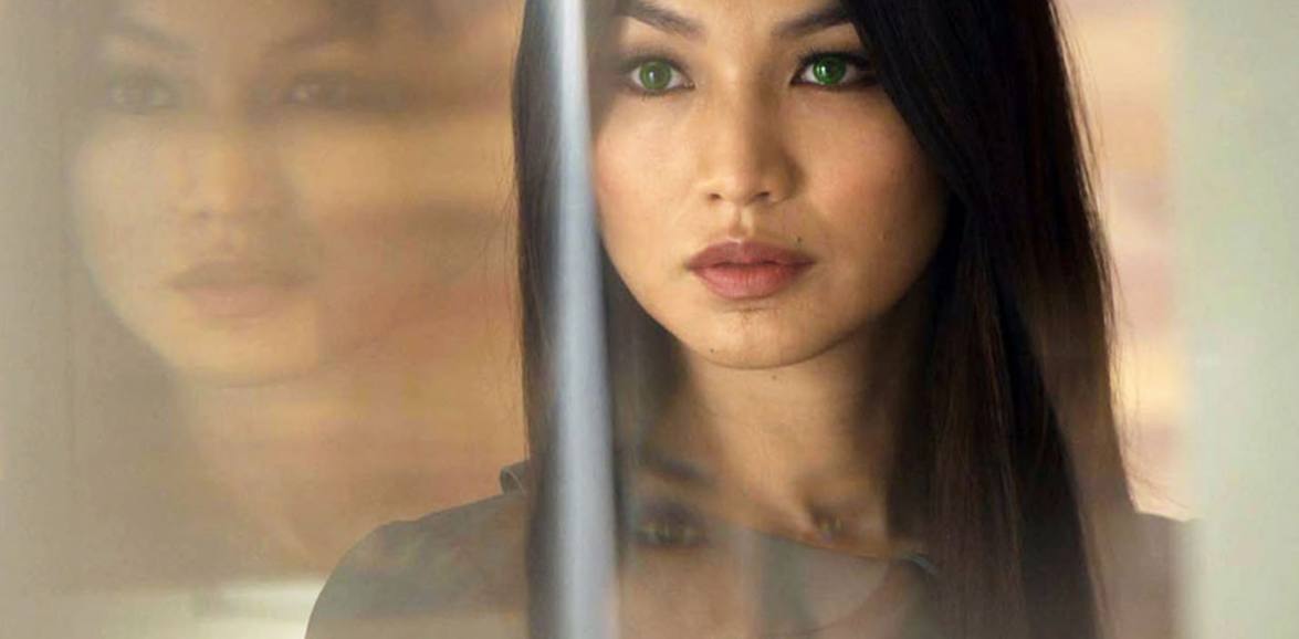 Close-up of Anita from Humans with luminous green eyes, her face reflected in glass.