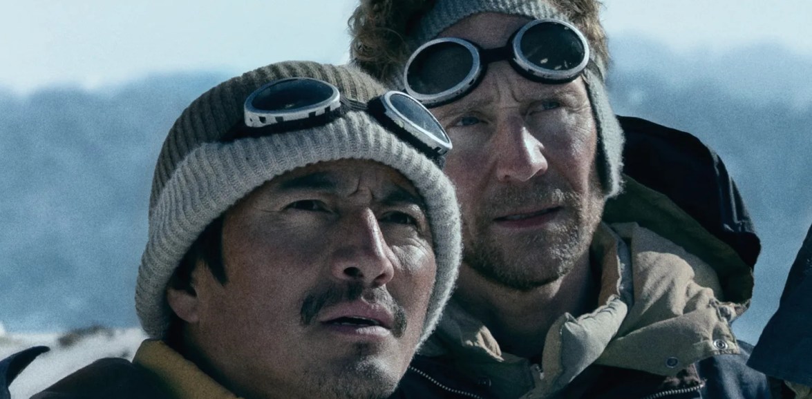 Tenzing Norgay and Edmund Hillary wearing woollen climbing hats and goggles as they look towards Everest.