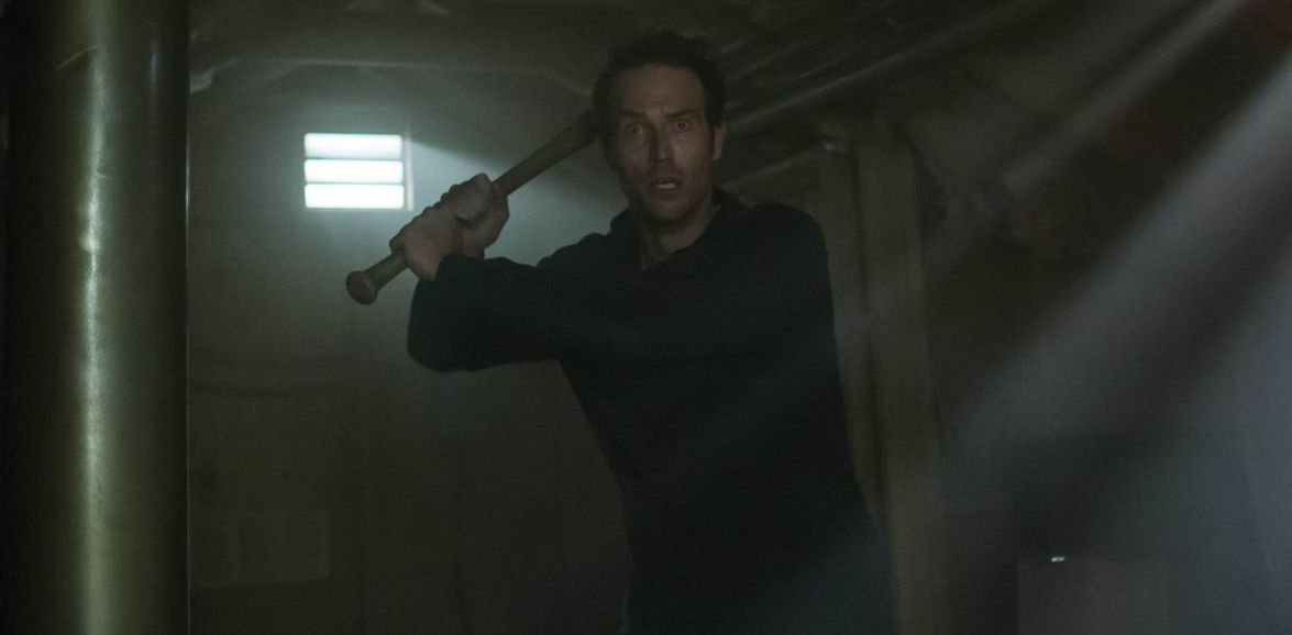 Michael Vartan as John Alexander searches a dark interior with a baseball bat in Within (2016).